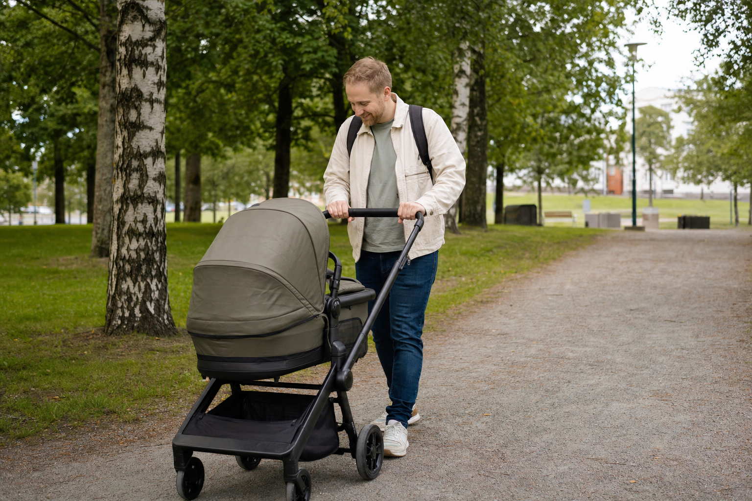 Isä työntää lastenvaunuja vehreässä suomalaisessa puistossa.