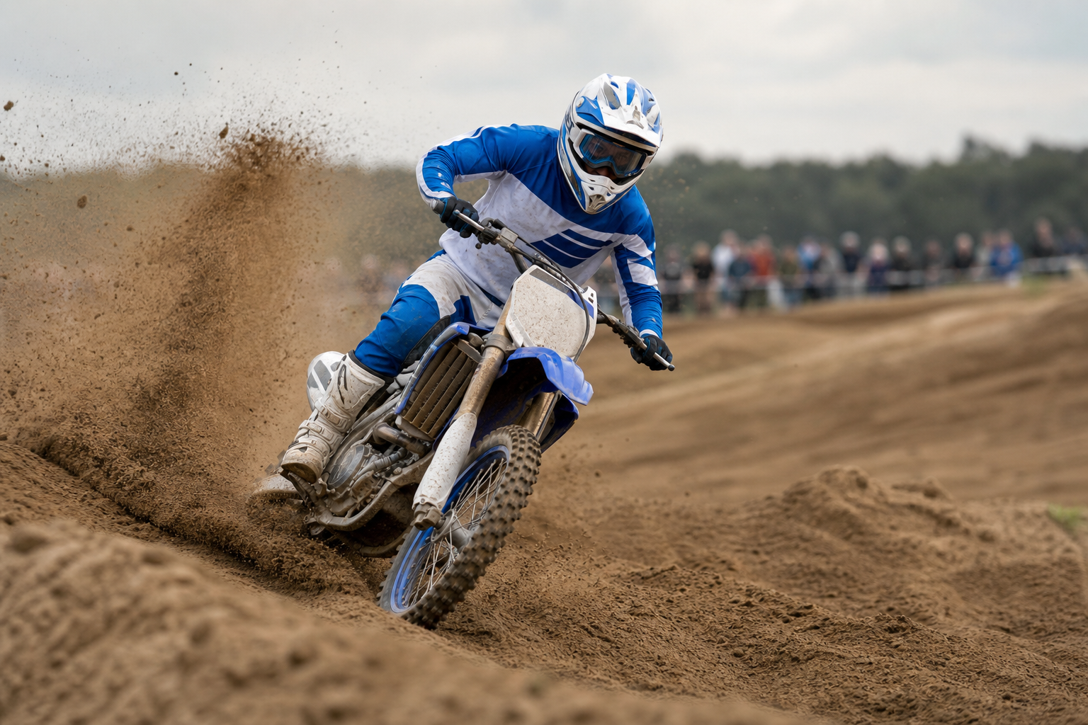 Kuvituskuva sinivalkoiseen ajoasuun pukeutuneesta motocrosskuljettajasta hiekkaradalla