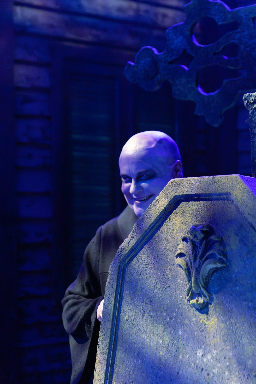 Kuopion kaupunginteatterin The Addams Family -tuotantokuva 27.8.2026: näyttämöhahmo hautakivilavasteen takana. Ei ensi-iltakuva.